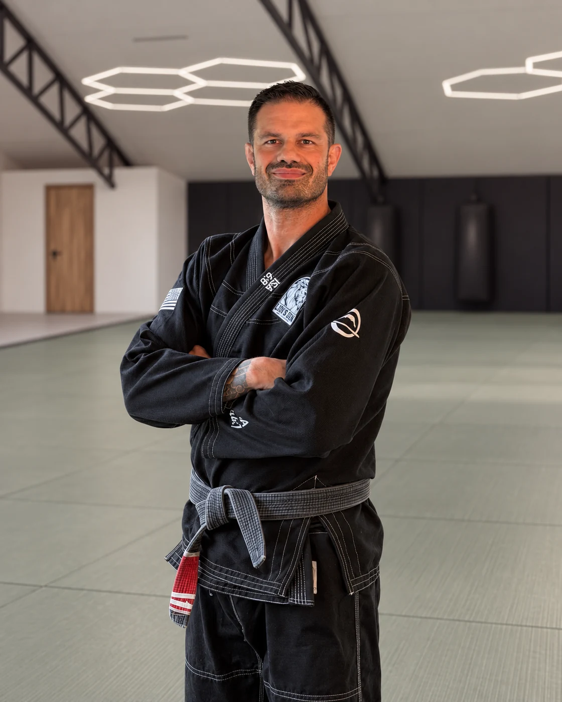 Jason Kalvesmaki in a black gi against a rendered Lion’s Den academy background